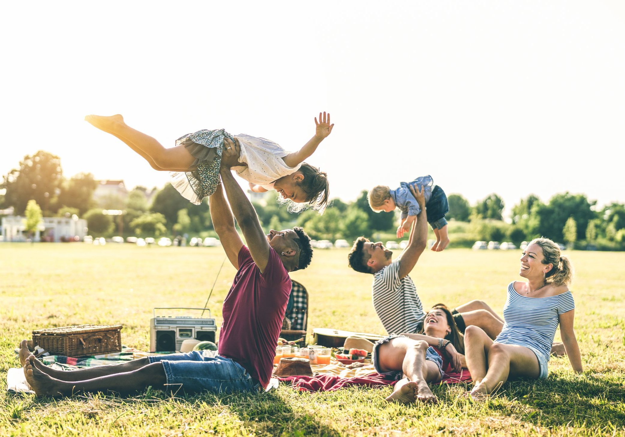 Young multiracial families having fun playing with kids at pic nic barbecue party - Multicultural joy and love concept with mixed race people together with children at park - Warm contrasted filter